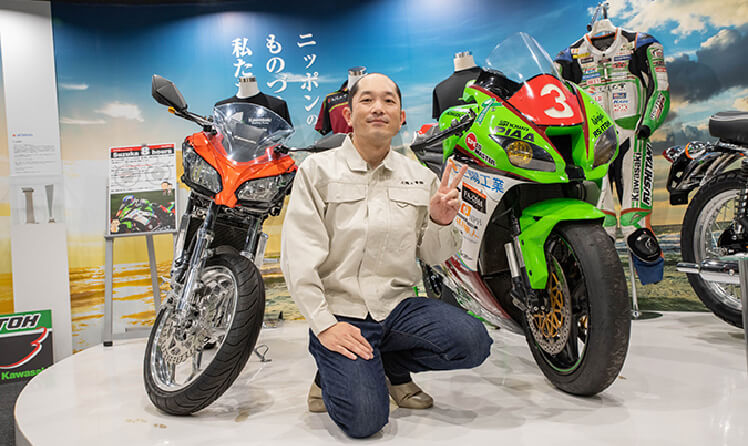 バイクの横でピースをしている 生産推進グループ社員